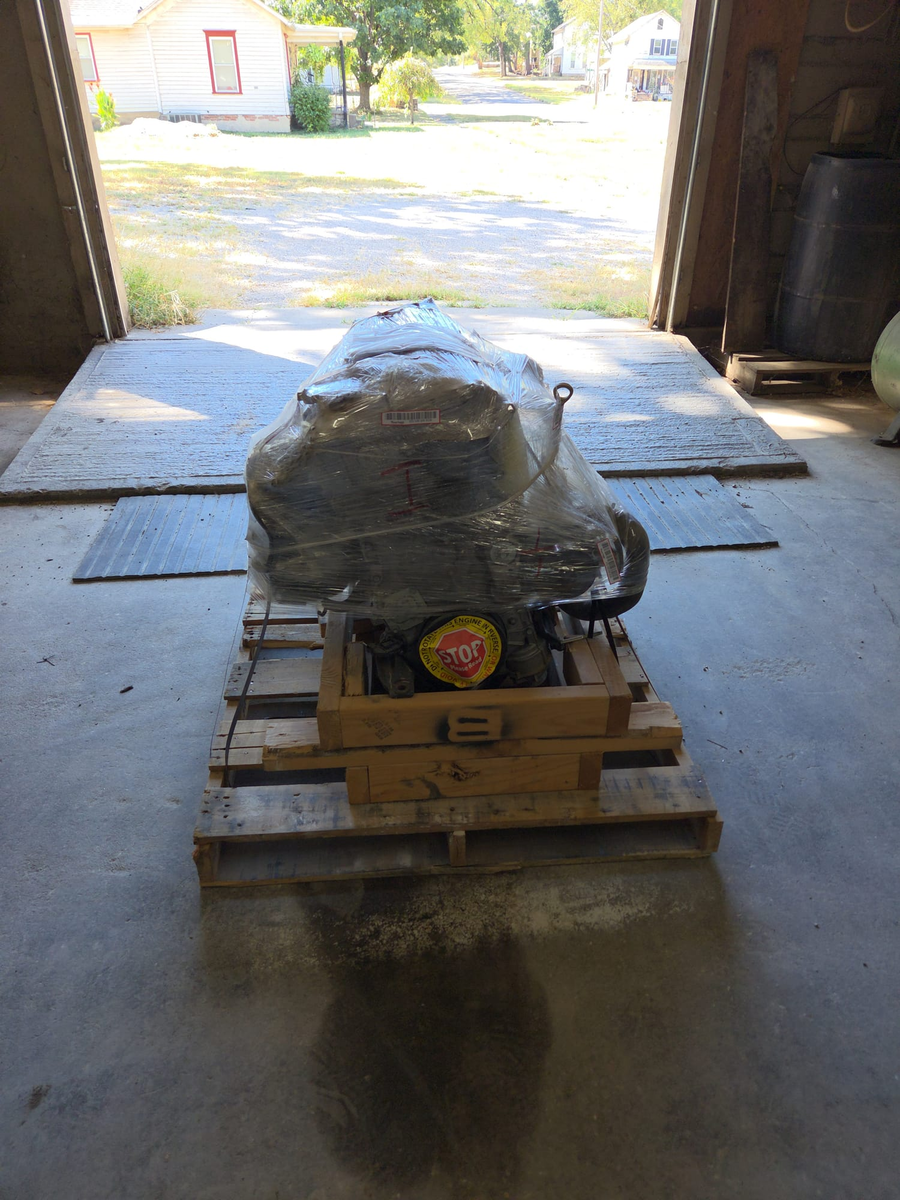 An engine wrapped in plastic on a wooden pallet, just inside the open shop door